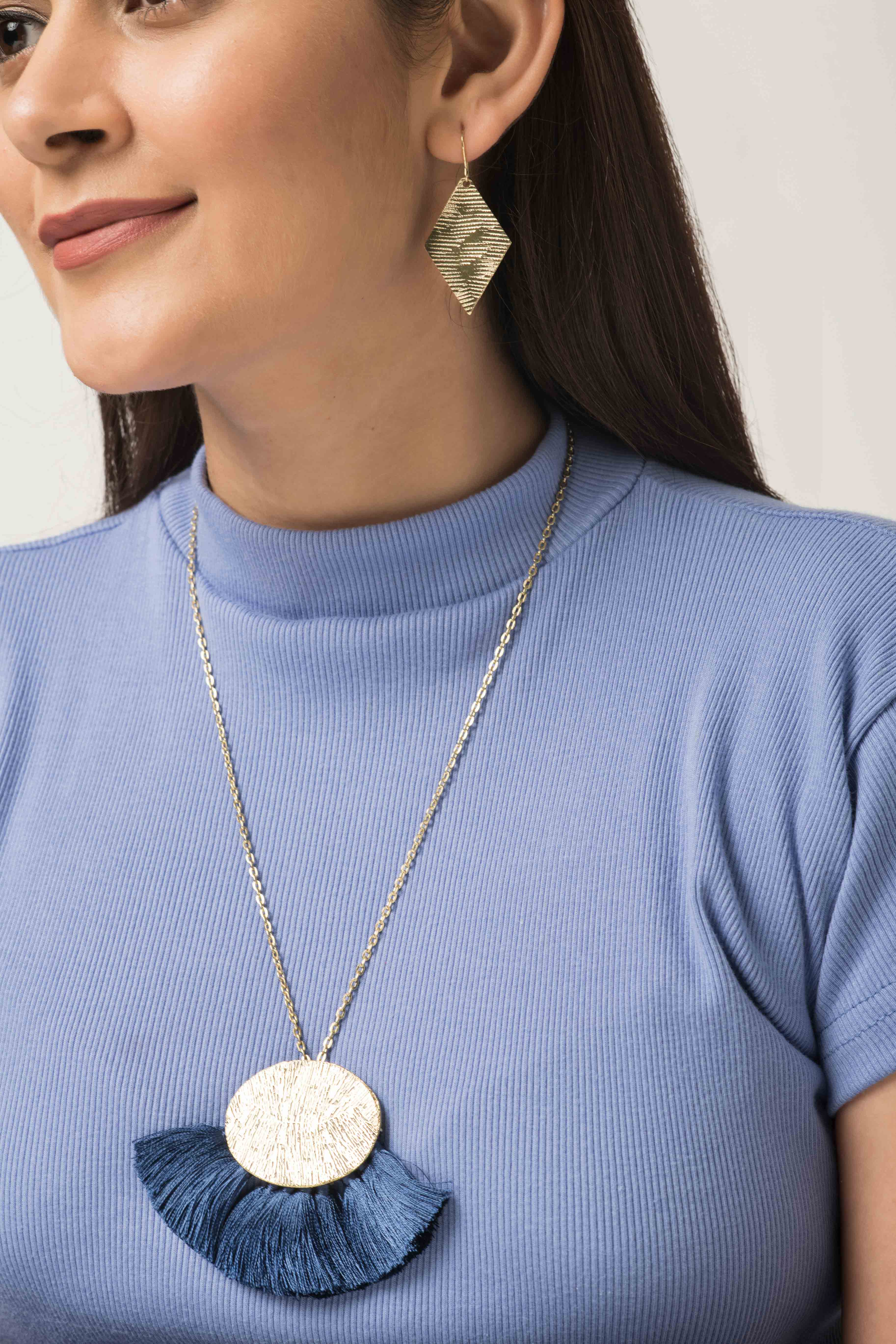 Woman wearing statement fair trade jewellery necklace. Large golden pendant with olive green tassels