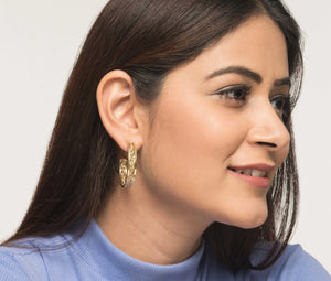 Woman wearing golden brass hoop earrings. Intricate design. Traditional methods. Sustainable fashion