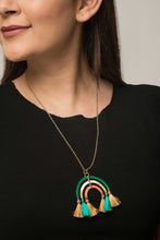 Woman wearing fairtrade brass necklace. Pendant is rainbow-like and has tassels. Sustainable fashion