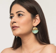 Woman wearing blue and gold brass ethical earrings with blue patina finish. Geometric shapes. 