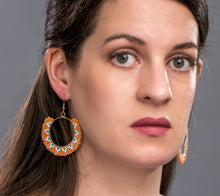 Woman wearing ring shaped drop earrings made of orange, blue, white glass beads. Ethical jewelry.