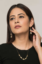 Woman wearing a set of earrings and necklace made of odd shaped golden beads and white wooden beads.