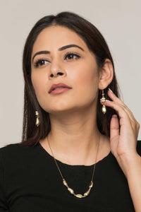 Woman wearing a set of earrings and necklace made of odd shaped golden beads and white wooden beads.