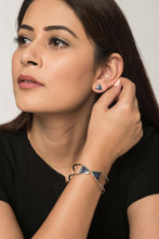 Woman wearing triangular grey and silver stud earrings and silver brass bracelet with grey tips.