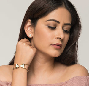Woman wearing triangular white and golden stud earrings and brass bracelet with white enamel tips. 