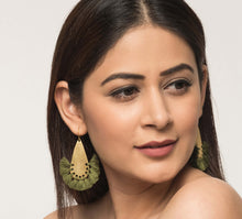 Woman looking stylish with golden statement brass earrings, finished with olive green tassels. 